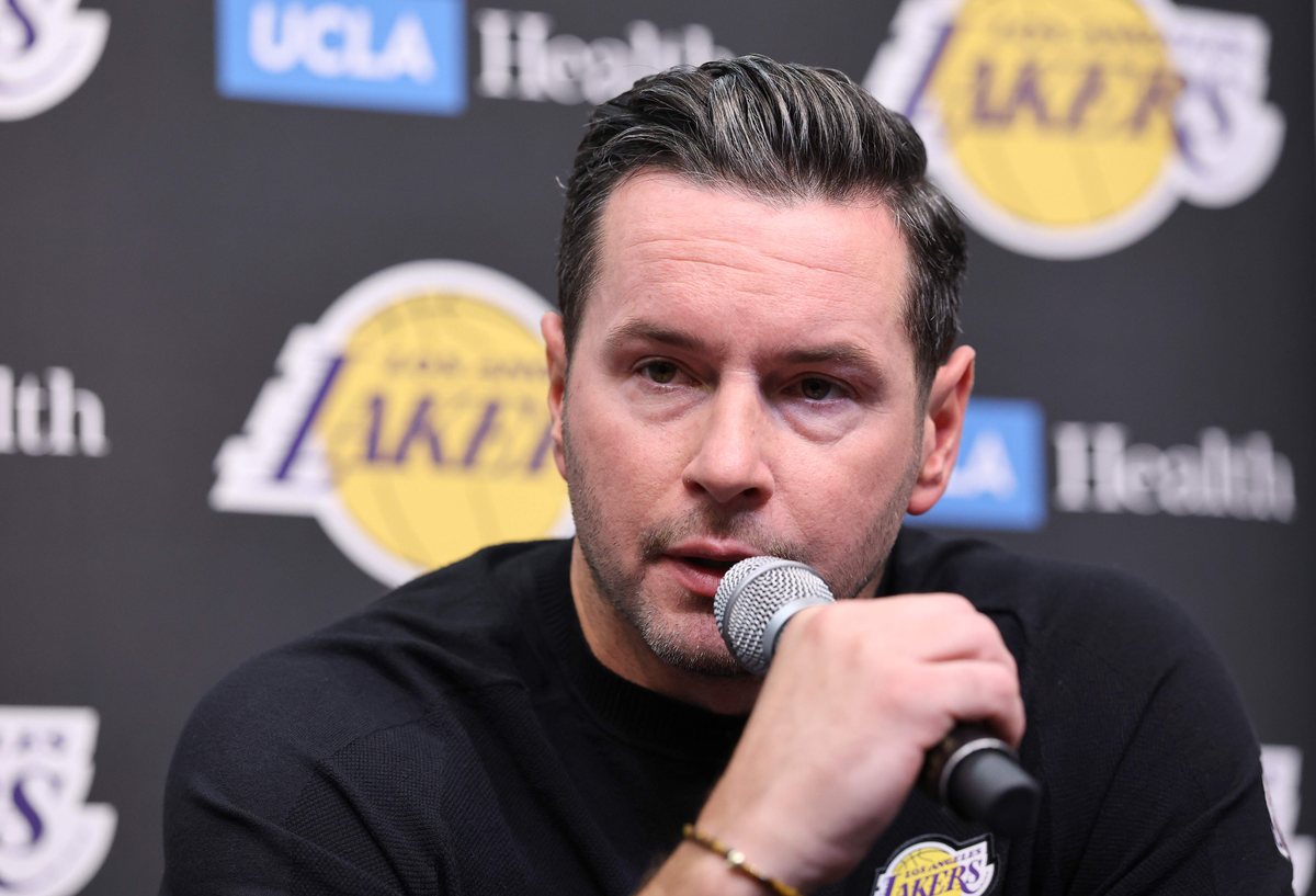 JJ Redick speaks into a microphone in front of a Lakers backdrop.