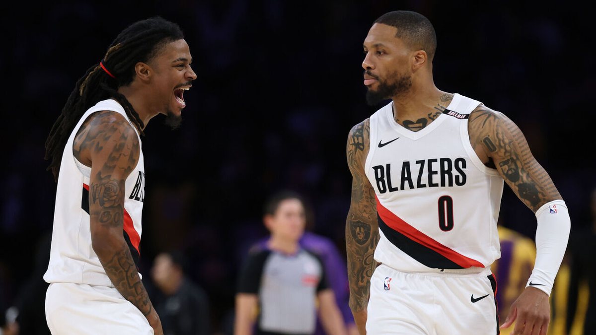 Ja Morant, shouting, and Damian Lillard, both in white Blazers jerseys, walk toward each other on the court.